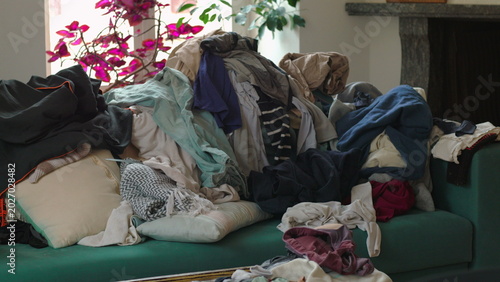 Foto Heaped garments layered across sofa near window and indoor plants portraying cha