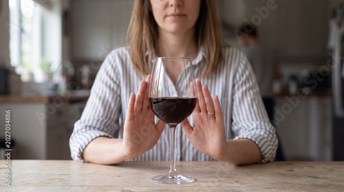 Woman refusing a glass of red wine at a kitchen table concept