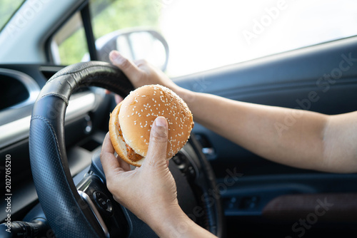 Obraz na płótnie Asian woman driver hold and eat hamburger in car, dangerous and risk an accident