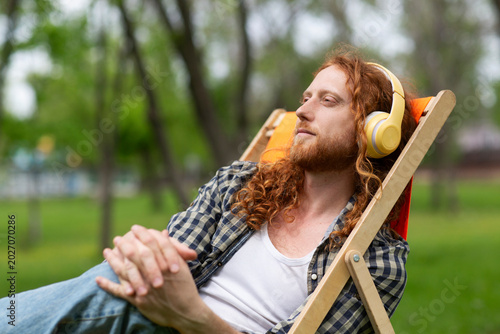 portrait of mature smiling man with red hairwith headphones resting and enjoying music sitting on a sun lounger in the garden on a summer day. concept without stress. mental health.  Enjoying the litt