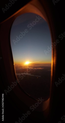 Beautiful golden sunset over dark landscape seen through airplane window portal during high altitude flight over China, sunburst shining on horizon with low cloud layer and large water reservoir.