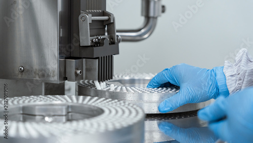 Industrial worker manages components on automated p. Modern pharmaceutical manufacturing facility and laboratory setup with colorful supplement capsules and high-tech automated production equipment.
