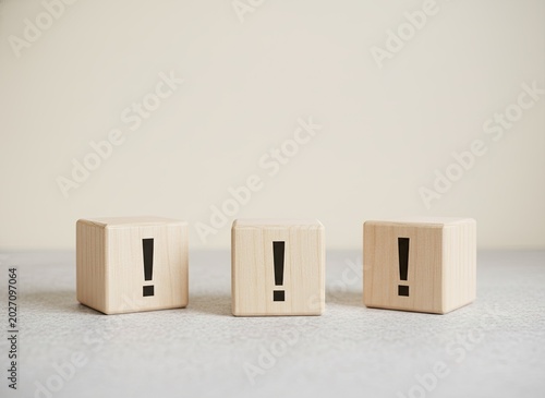 Three wooden blocks each featuring a printed exclamation mark displayed on a smooth textured surface