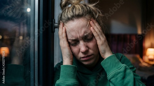 Distressed blonde woman holds her head with hands expressing emotional pain or stress