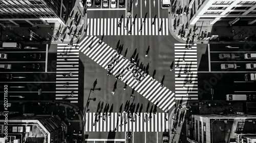 Overhead black and white view of a busy city intersection with pedestrians crossing multiple crosswalks and cars