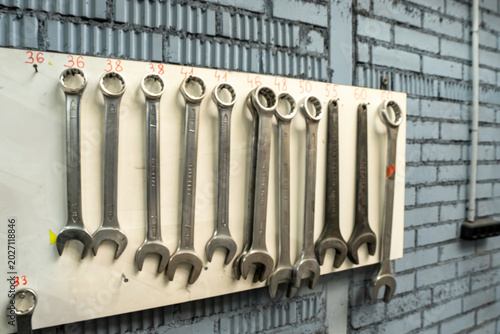 Organized set of professional wrenches and sockets on a tool board in an auto repair shop. Mechanical tools hanging on a white wall organizer in a garage with industrial brick background.