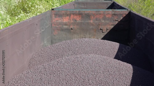 Open freight train wagons loaded with metal pellets or iron ore balls moving along industrial railway tracks. Heavy industry transportation and mining logistics concept.