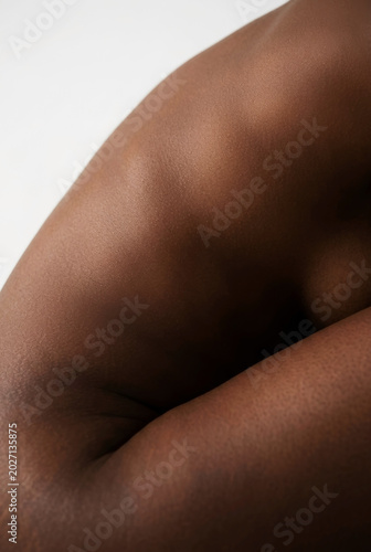 Abstract, artistic close-up of dark-toned skin curves, highlighting soft lighting and texture