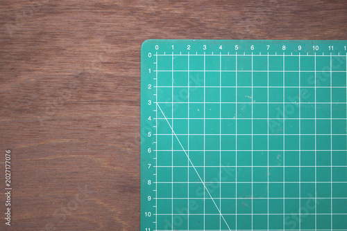 Green cutting mat with grid lines positioned on a wooden table, suggesting crafting, sewing, model making, and organized workspace for DIY projects and design work.