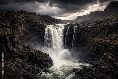 Impressive waterfall tumbling through volcanic rock formations surrounded by a dramatic wilderness under stormy skies
