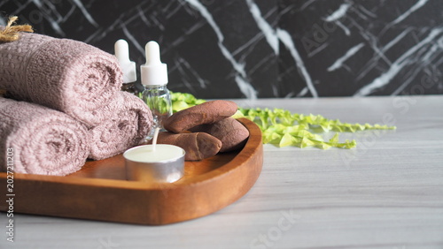 Photography Spa wellness composition with rolled towels, essential oil dropper bottles, massage stones and candle on wooden tray