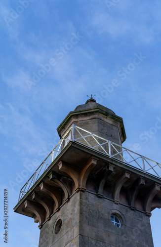 The stone lighthouse is in the classical style against blue sky. The building is designed in the classical style, with balcony