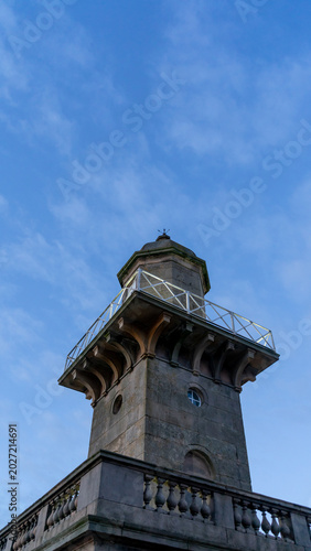 The stone lighthouse is in the classical style against blue sky. The building is designed in the classical style, with balcony