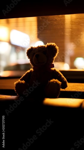 Brown teddy bear sitting on car seat at night with city lights.