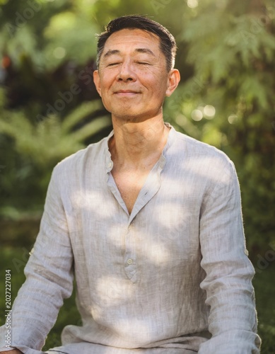 Middle-Aged Man Meditating Outdoors in Golden Sunlight Among Lush Garden Foliage