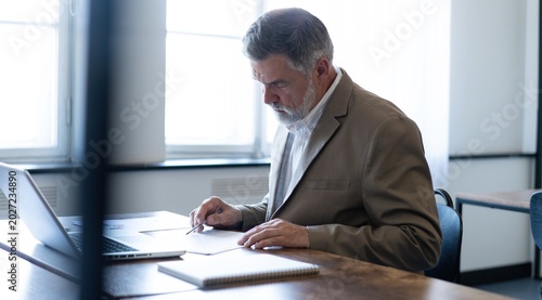 Mature businessman working with document in modern office, reading contract, analyzes graph
