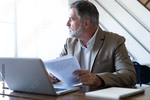 Mature businessman working with document in modern office, reading contract, analyzes graph