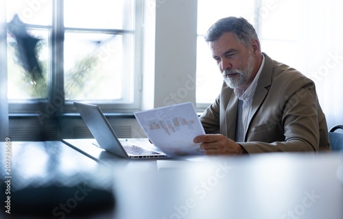 Mature businessman working with document in modern office, reading contract, analyzes graph