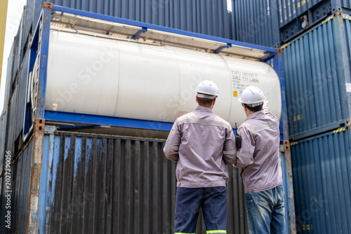 Male engineers in safety helmets discussing and inspecting gas tank container at logistics shipping port terminal site
