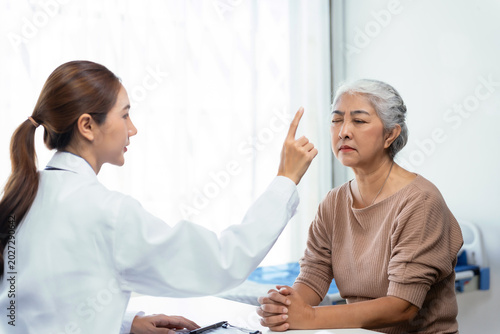 Doctor performing a neurological checkup on a senior woman, testing her vision and eye movement in a clinic