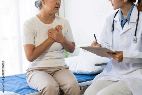 Senior woman suffering from chest pain during a medical consultation with a female doctor, discussing symptoms and healthcare for elderly patients