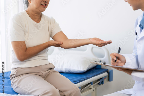 Senior woman patient consulting doctor about elbow injury. Healthcare professional writing medical notes during hospital check up