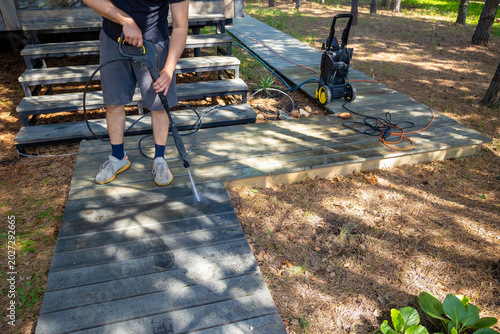 Cleaning wooden garden pathway with pressure washer near forest cabin. Concept: backyard care.