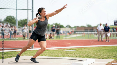 Female athlete throwing shot put in track and field stadium. Strong woman in mid-motion during throwing event. Athletic competition concept