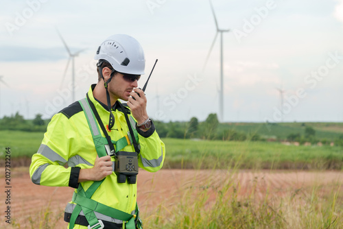 Caucasian male engineer wearing protective uniform communicates by radio during wind turbine maintenance task at wind farm supporting renewable electricity generation sustainable energy technology
