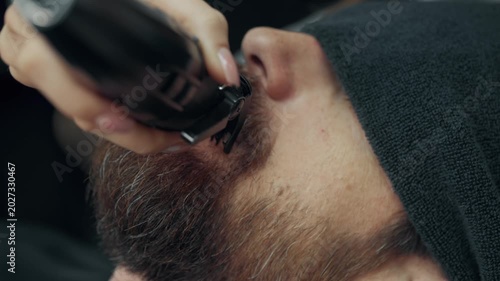 Close up of barber trimming mustache with electric clipper during beard grooming procedure in modern barbershop