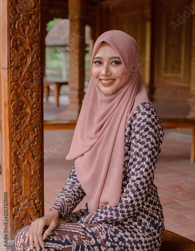 Smiling Muslim Woman Wearing Hijab and Batik Dress in Traditional Wooden Indonesian Pavilion Portrait