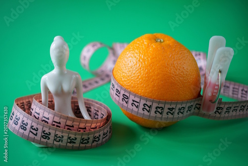 A ceramic statuette of a woman in the lotus position and an orange with a centimeter.  Diet, fitness, and weight loss.
