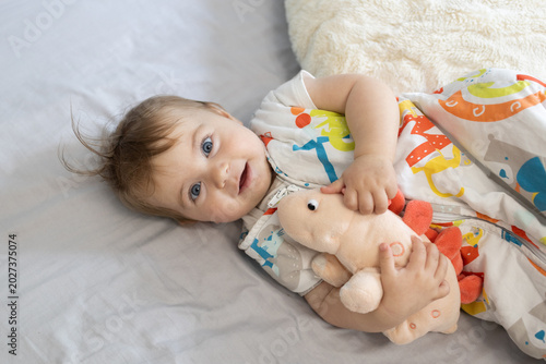 Photography cute baby with a pink dinosaur toy in a sleeping bag wakes up and lies on her bed at home