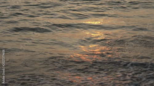 Golden Sunlight Reflects on Gentle Ripples of Calm Sea and Ocean Waves, Creating Serene and Tranquil Beach Scene with Water Reflection