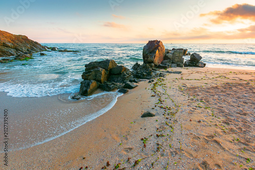 huge stones on the sandy beach at sunrise. wonderful holiday season background at the sea. clouds on the blue sky above horizon. view of waves washing the shore. scenic seascape for relaxation