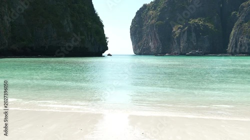 Serene Tropical Beach with Clear Turquoise Water and Towering Cliffs Under Bright Sky Creating Tranquil Paradise
