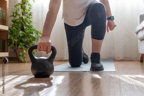 Cuadro en lienzo Mature woman in activewear doing a kneeling kettlebell lunge in her living room,