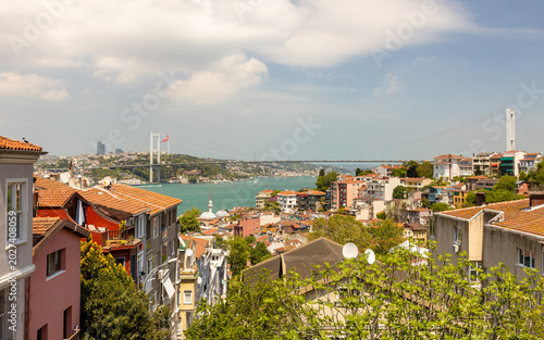 Panoramic view of Istanbul cityscape with traditional houses, the Bosphorus strait, and the Bosphorus Bridge under a cloudy sky