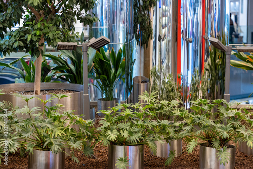 Modern eco-friendly indoor landscaping with green potted plants, trees, and LED grow lights in a contemporary urban public space.