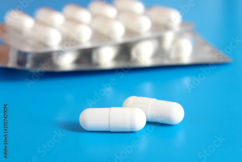 On a blue background lies a blister pack with white medicine capsules.