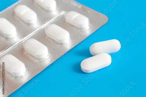 On a blue background lies a blister pack with white oblong tablets.