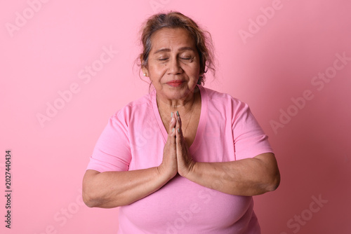 Obraz na płótnie Peaceful Senior Latina Woman Praying on Pink Background