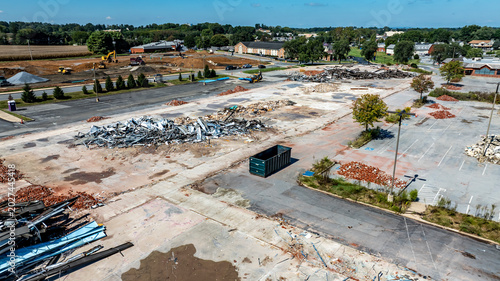 The scene shows a construction area with piles of debris and rubble from a demolished building. Heavy machinery is present, clearing the site. The weather is clear with a blue sky.