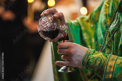 Photos Priest pouring red wine from crystal decanter into chalice.
