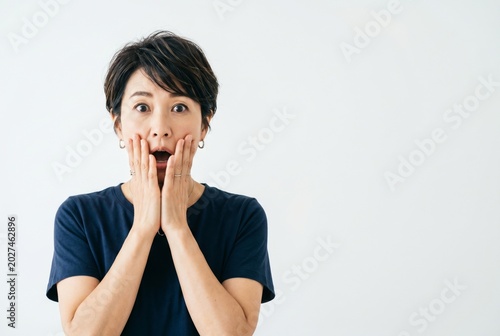 A surprised middle-aged Asian woman in a T-shirt on a white background. Space for text