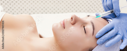 Bild auf Leinwand A woman lies on a treatment table while a cosmetologist applies a beauty procedure using a syringe