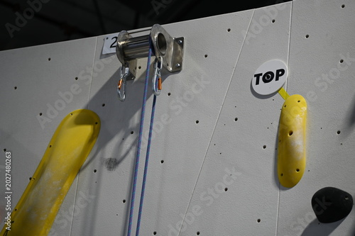 Top of an indoor rock-climbing wall with yellow holds and carabiners