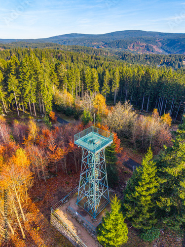 Slovanka Lookout Tower, the oldest iron tower in the Czech Republic, rises above the colorful autumn landscape of Jizera Mountains. Trees in vibrant hues surround this historic landmark.