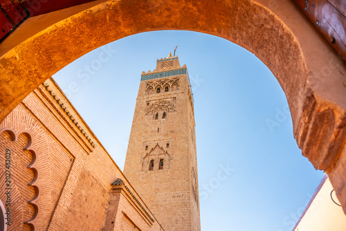 Koutoubia Mosque stands tall in Marrakech  Morocco. The image shows the mosque tower viewed through an archway. Clear blue sky is visible above the building.