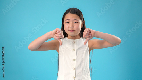 Canvastavla Upset crying young asian girl looking at camera showing thumbs down